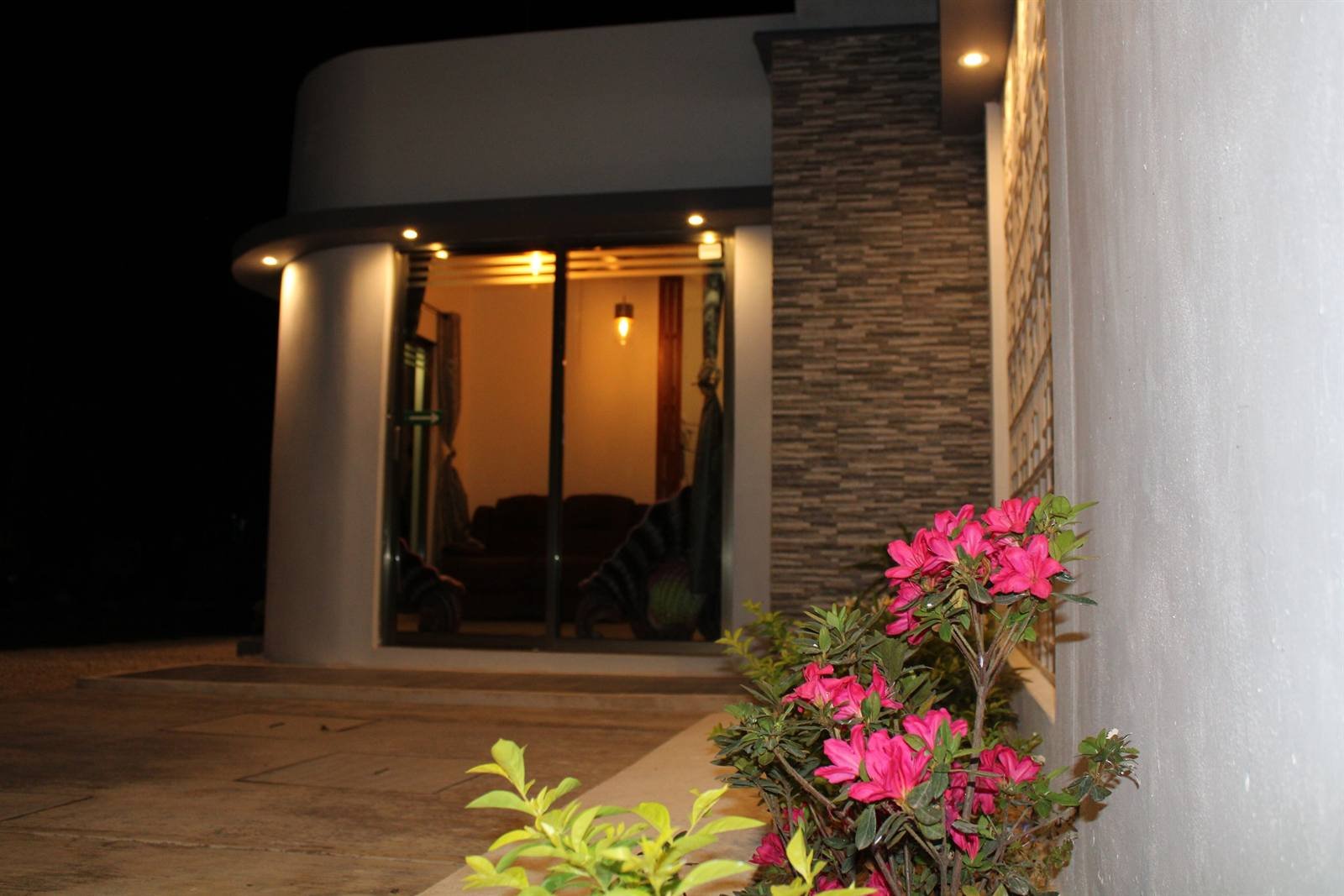 Casa Zazil's entrance lit up at night, with pink flowers in the foreground