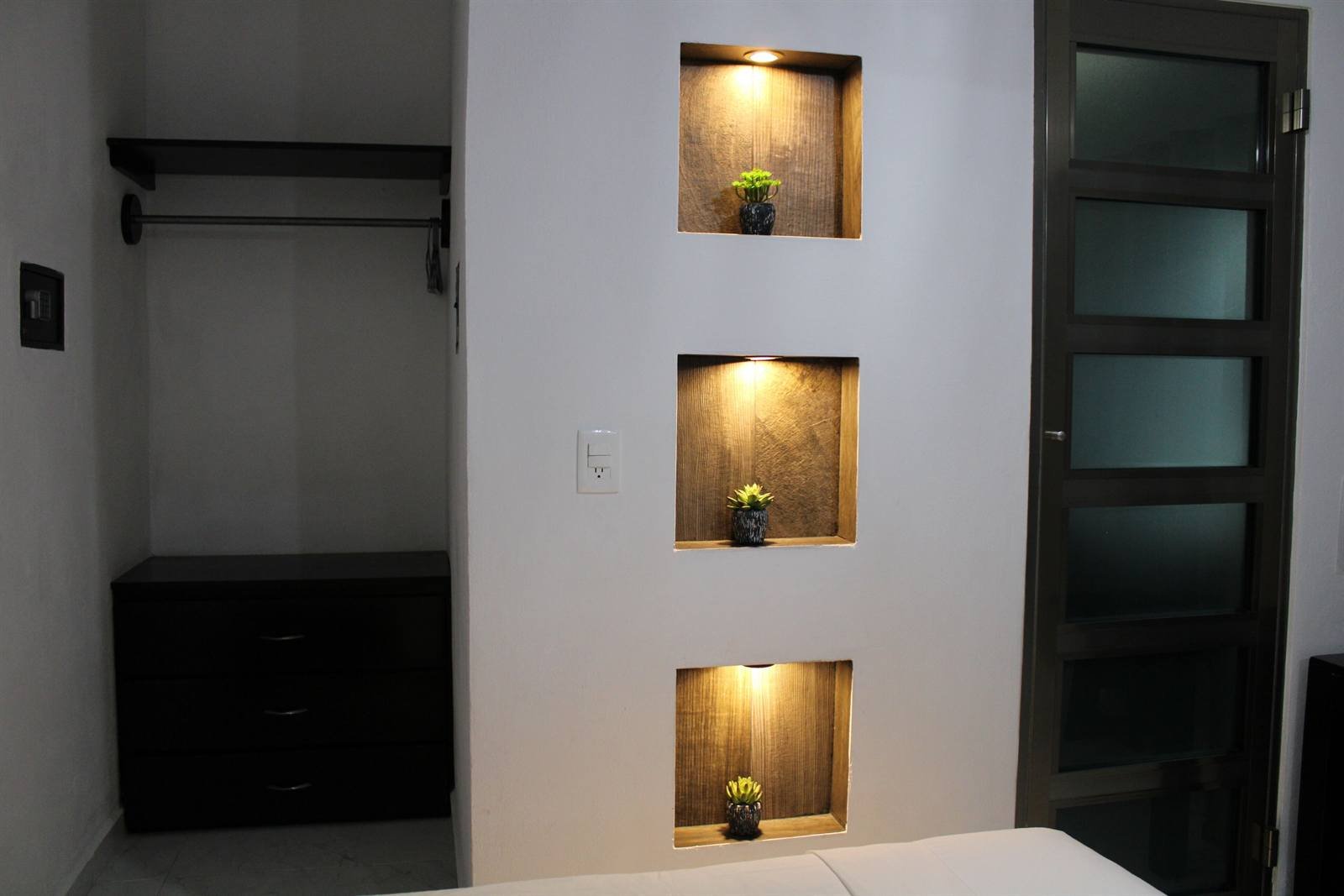 Room detail with a closet rail, dresser and lit shelves with small plants